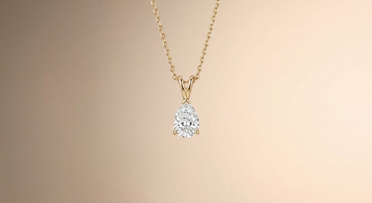 A single gold pendant necklace with a pear-cut diamond, photographed alone against soft warm negative space.